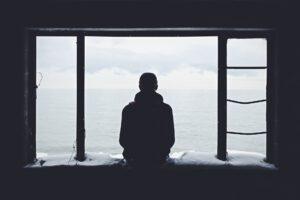 Man sits on a window sill, looking out, pensive.