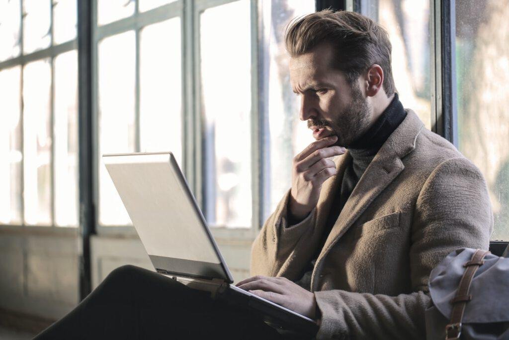 A man looking at an open laptop with doubt