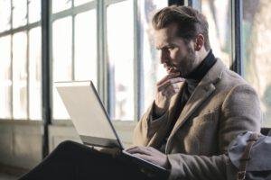 A man looking at an open laptop with doubt